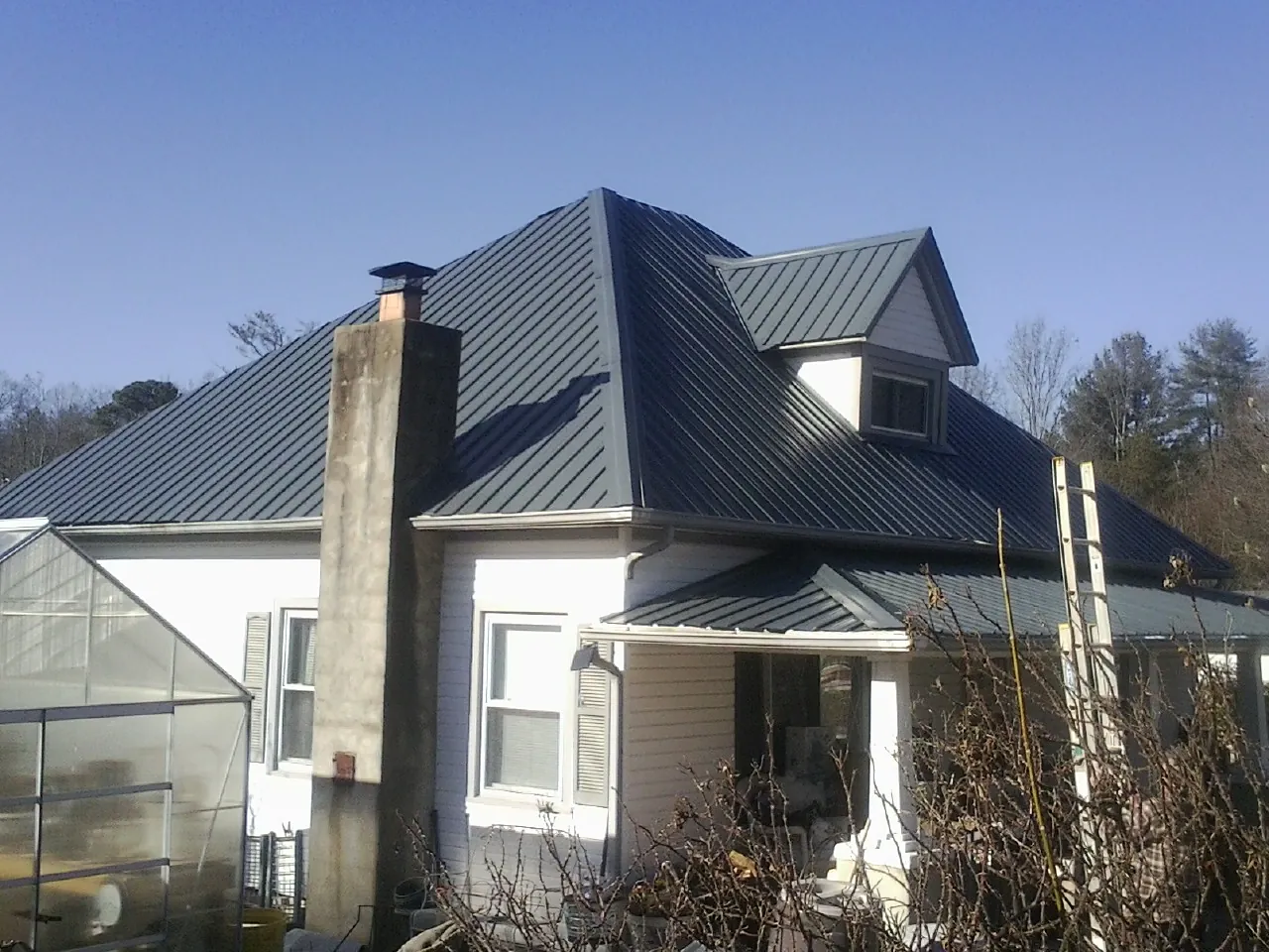 Dark blue standing seam metal roof on a white farmhouse with dormer — Slate & Tile Roof Repair by Roofing Brothers in Hailey