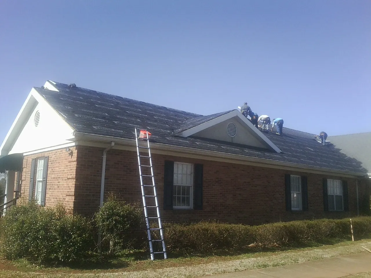Crew tearing shingles off a brick ranch roof with a ladder set — Emergency Roof Repair work by our crew in Hailey