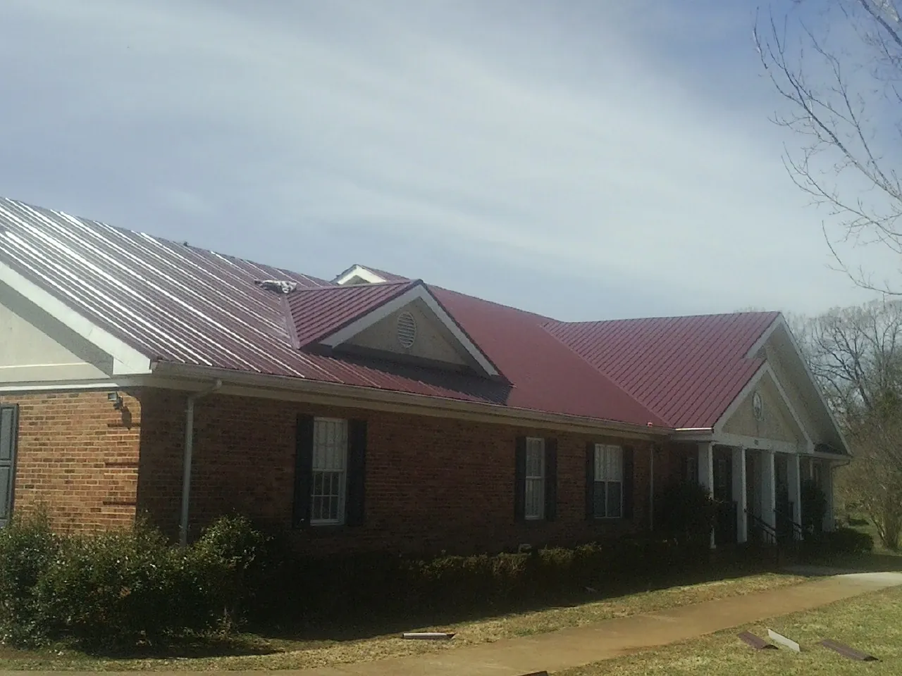 Red metal roof with gabled entries on a long brick building, from a Hail Damage Roof Repair job in Hailey