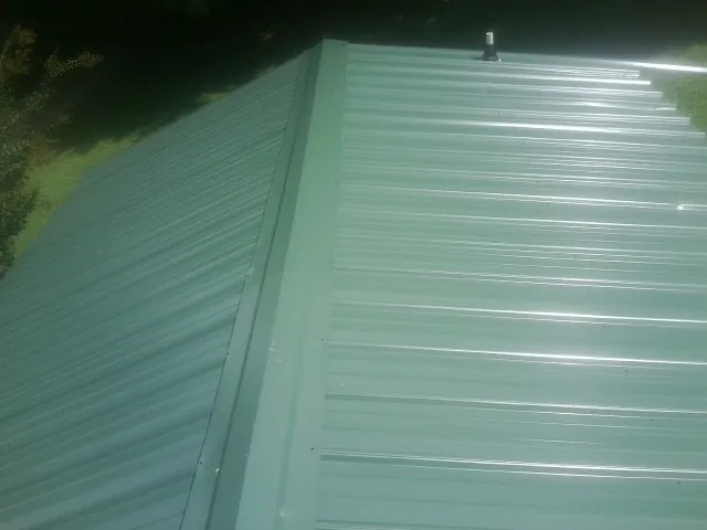 New green metal panels meeting at the ridge of a roof — Flat Roof Repair work by our crew in Hailey
